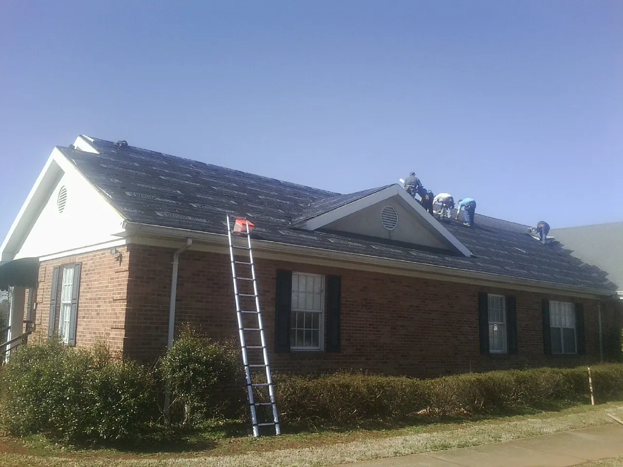 Crew tearing shingles off a brick ranch roof with a ladder set — Emergency Roof Repair work by our crew in Pleasureville