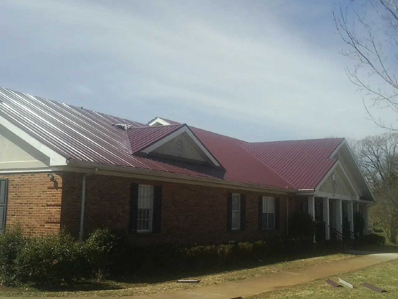 Red metal roof with gabled entries on a long brick building, from a Hail Damage Roof Repair job in Pleasureville
