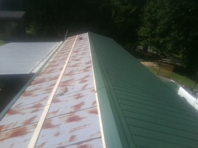Old rusted panels beside newly installed green metal roofing — Wind Damage Roof Repair by Roofing Brothers in Pleasureville