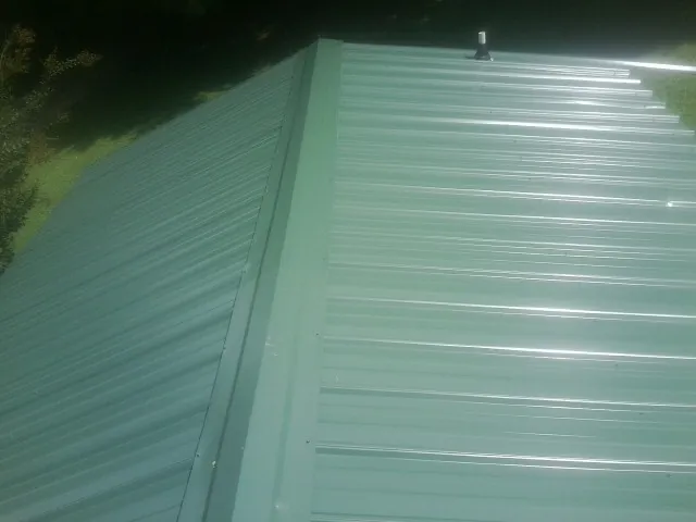 New green metal panels meeting at the ridge of a roof — Flat Roof Repair work by our crew in Pleasureville