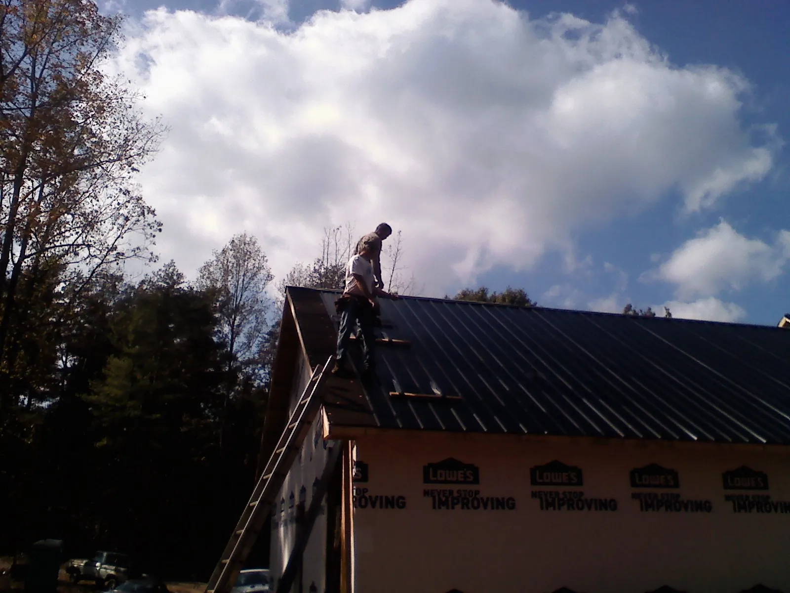 Roofer fastening dark metal panels high against a cloudy sky, from a Roof Inspection job in Pleasureville