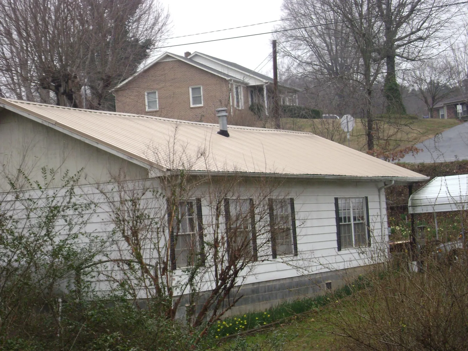 Tan metal roof on a white sided house set into a hillside — Commercial Roofing by Roofing Brothers in Pleasureville